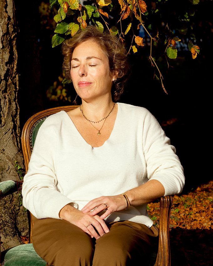 Luisa assise dans un fauteuil sous un arbre, les yeux fermés, dans la lumière du soir